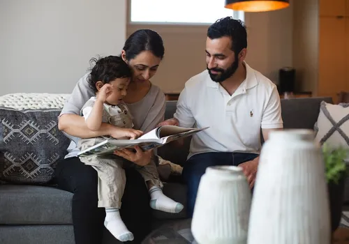 A young father and mother holding a child in their home, reading a book.